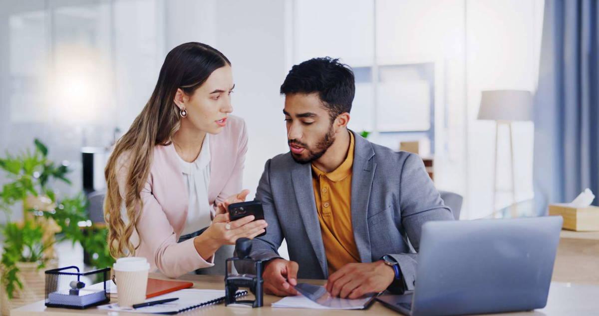 Two business professionals reviewing text messages in business strategy on smartphone and laptop using MoceanAPI in a modern office environment