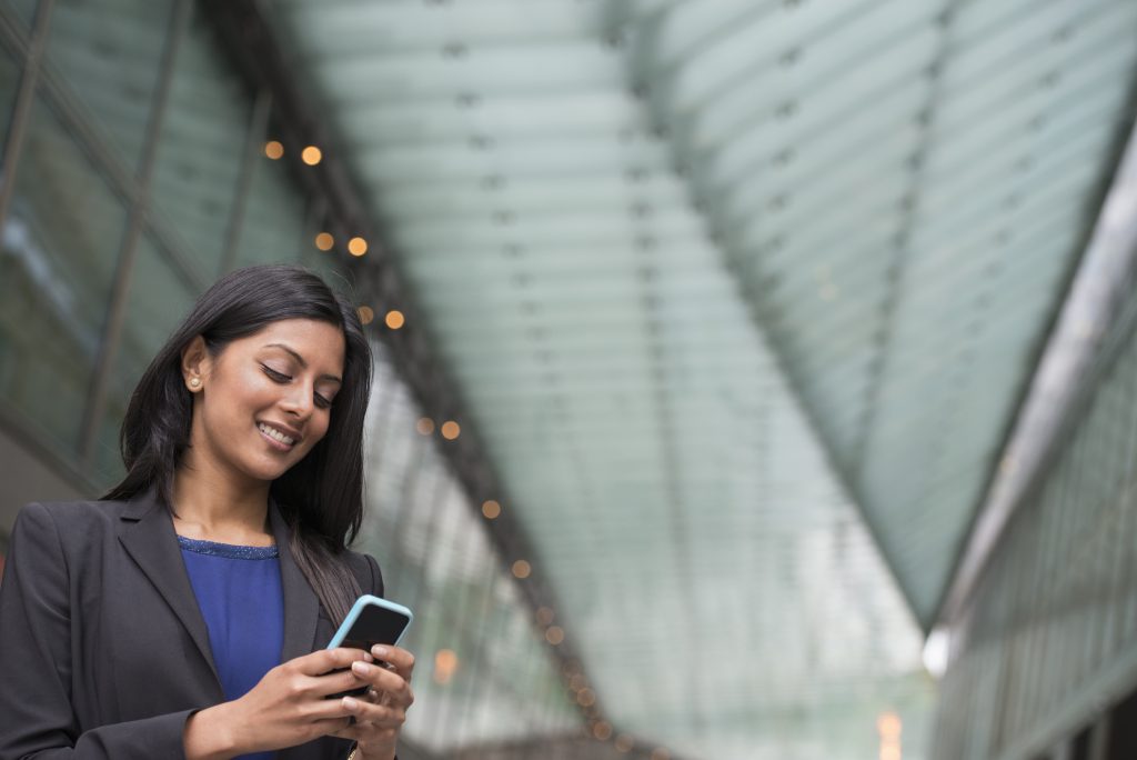 A professional businesswoman smiling while using her smartphone, representing seamless communication with a reliable SMS Gateway Provider.