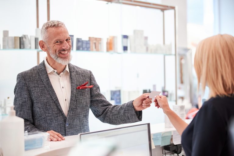 A smiling customer receiving a loyalty card from a staff member at a modern retail counter, symbolizing personalized service and customer engagement through SMS Service Malaysia.