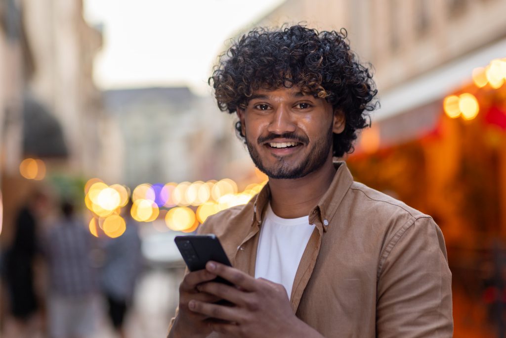 Two cheerful young professionals using smartphones outside a modern office, representing mobile-focused communication in SMS marketing Malaysia.