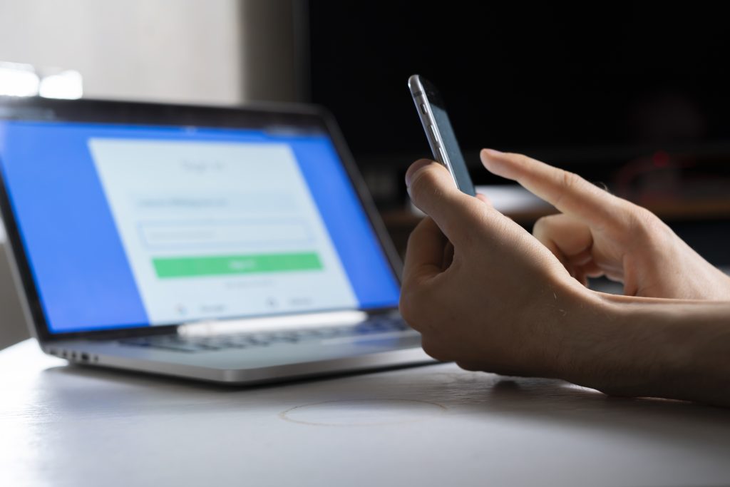 Hand holding a phone while logging into a web app on a laptop, illustrating SMS API usage