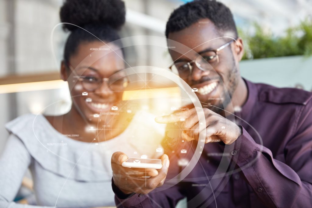 Two people smiling while interacting with a smartphone, representing how programmable SMS APIs deliver messages to end users' phones.