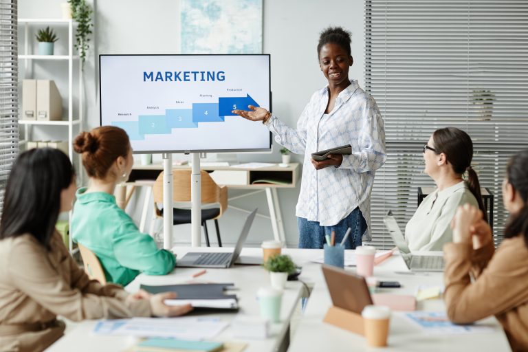 A businesswoman presenting a Bulk SMS Malaysia marketing strategy to a group of colleagues during a team meeting.