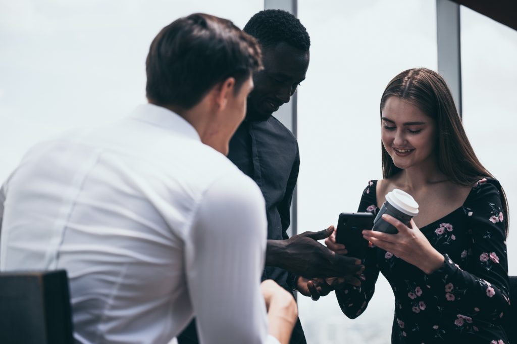 Three professionals reviewing a smartphone—team evaluating campaigns with the Best SMS Service Provider.