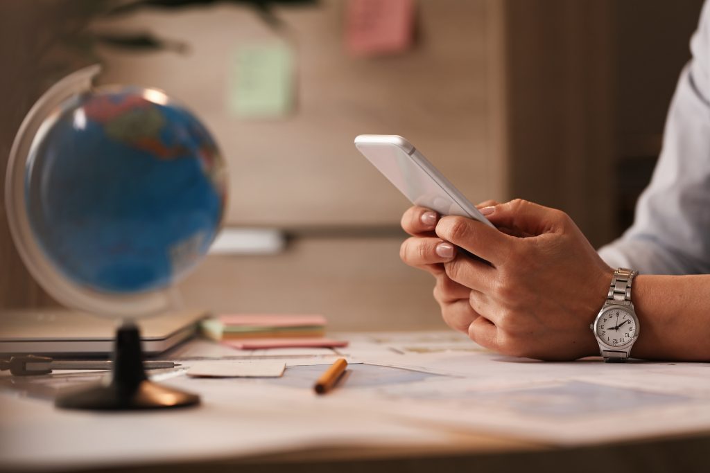 A businesswoman using a smartphone to expand her business's global reach with an SMS API Malaysia, with a world globe in the background.