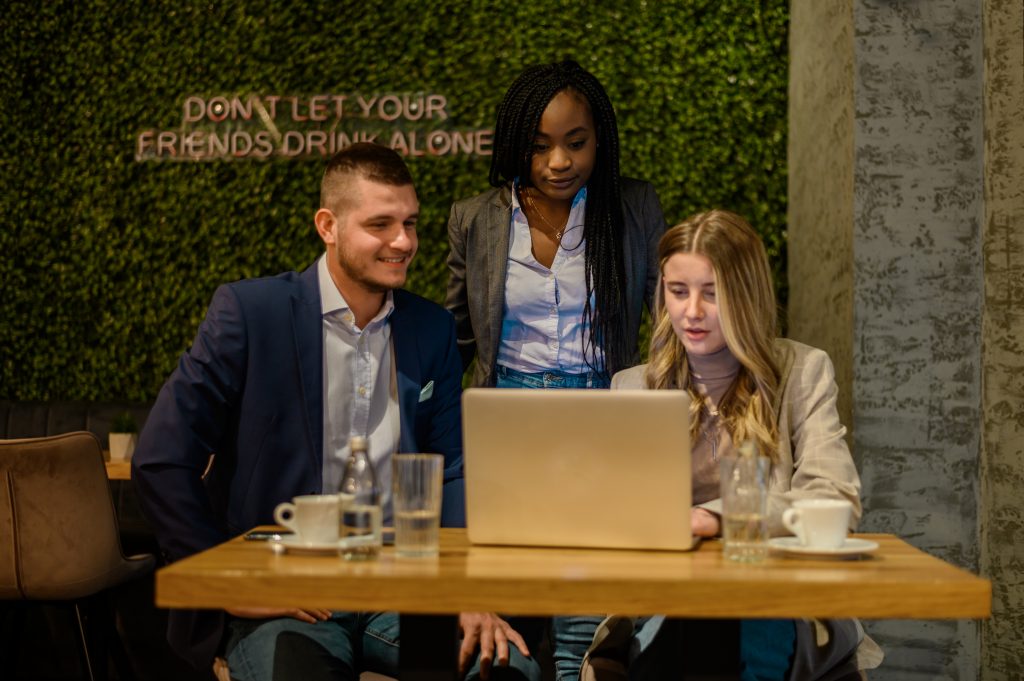 Three colleagues collaborate at a laptop in a café, planning personalized campaigns with a send SMS API.