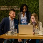 Three colleagues collaborate at a laptop in a café, planning personalized campaigns with a send SMS API.