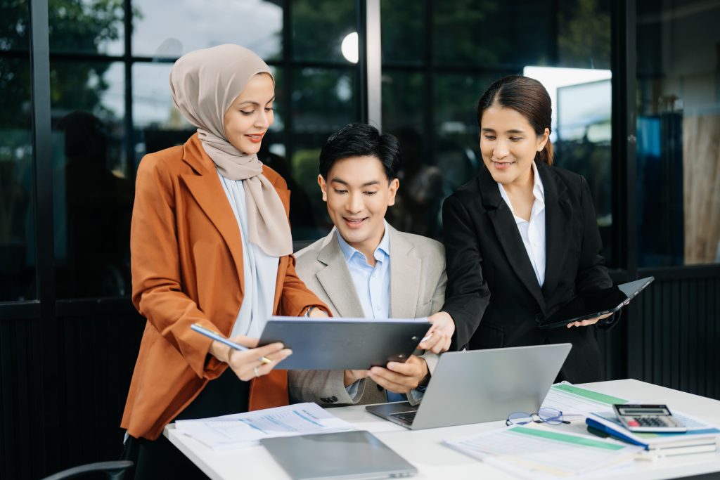 Marketing team collaborating around a laptop, planning a bulk SMS Malaysia campaign and reviewing analytics in a modern office.