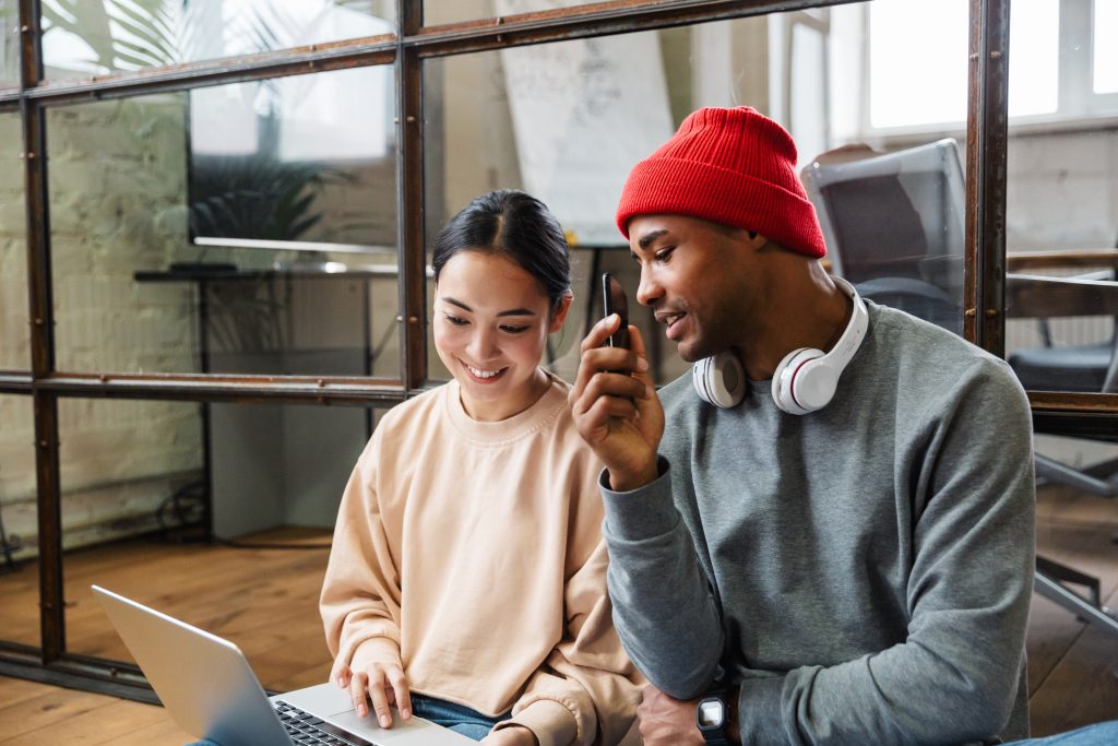 Two diverse colleagues collaborating in a modern office, happily reviewing a mobile campaign on a smartphone, illustrating the ease of use of a Bulk SMS Malaysia service for business communication.