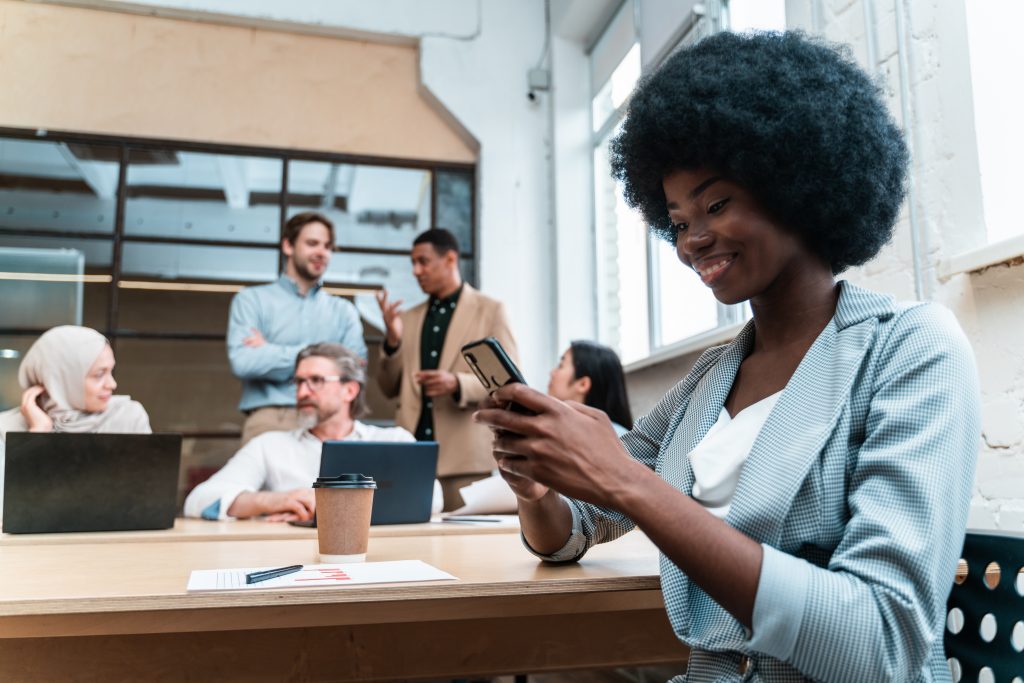 Programmable SMS API testing in a modern office—woman on a phone while teammates collaborate, illustrating two-way messaging vs traditional gateways.