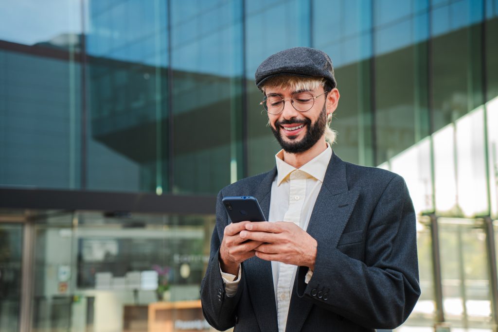 Young professional man using smartphone outside modern office — representing how businesses connect with customers through SMS gateway providers in 2025.