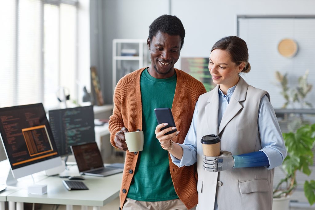 Two colleagues smiling while checking a smartphone, illustrating messaging API vs SMS in modern business communication.