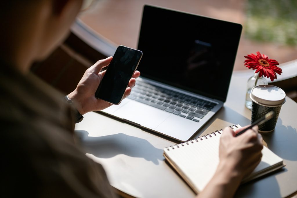 Business person comparing SMS Marketing Malaysia and email strategies using a smartphone and laptop at a cafe