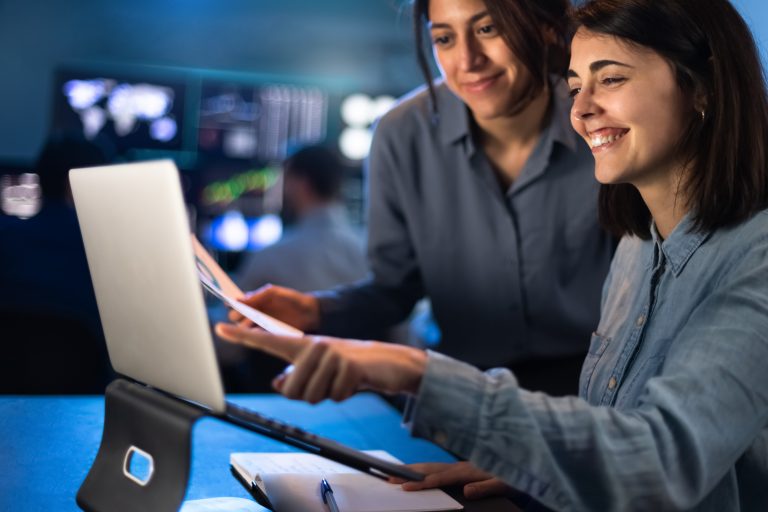 Two professionals collaborating on a laptop while discussing how a Programmable SMS API improves customer communication and business efficiency.