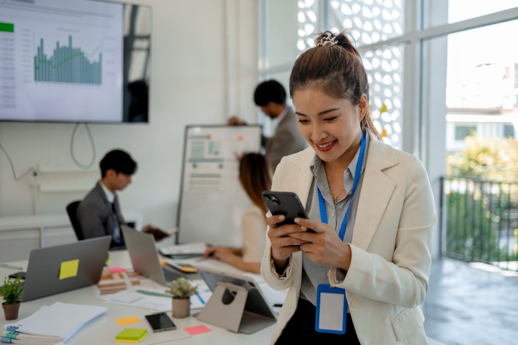 A businesswoman smiling while checking her phone in a modern office, representing global messaging success with the Best SMS Service Provider.