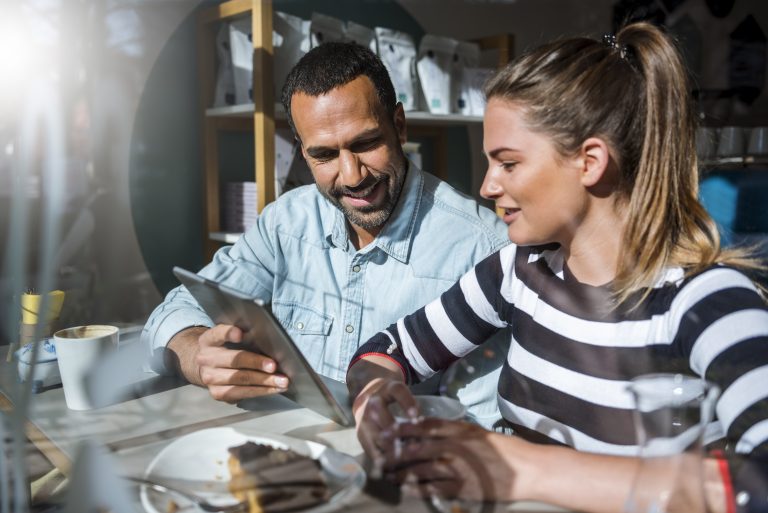 Two people using a tablet in a café discussing customer communication and SMS API Malaysia solutions.