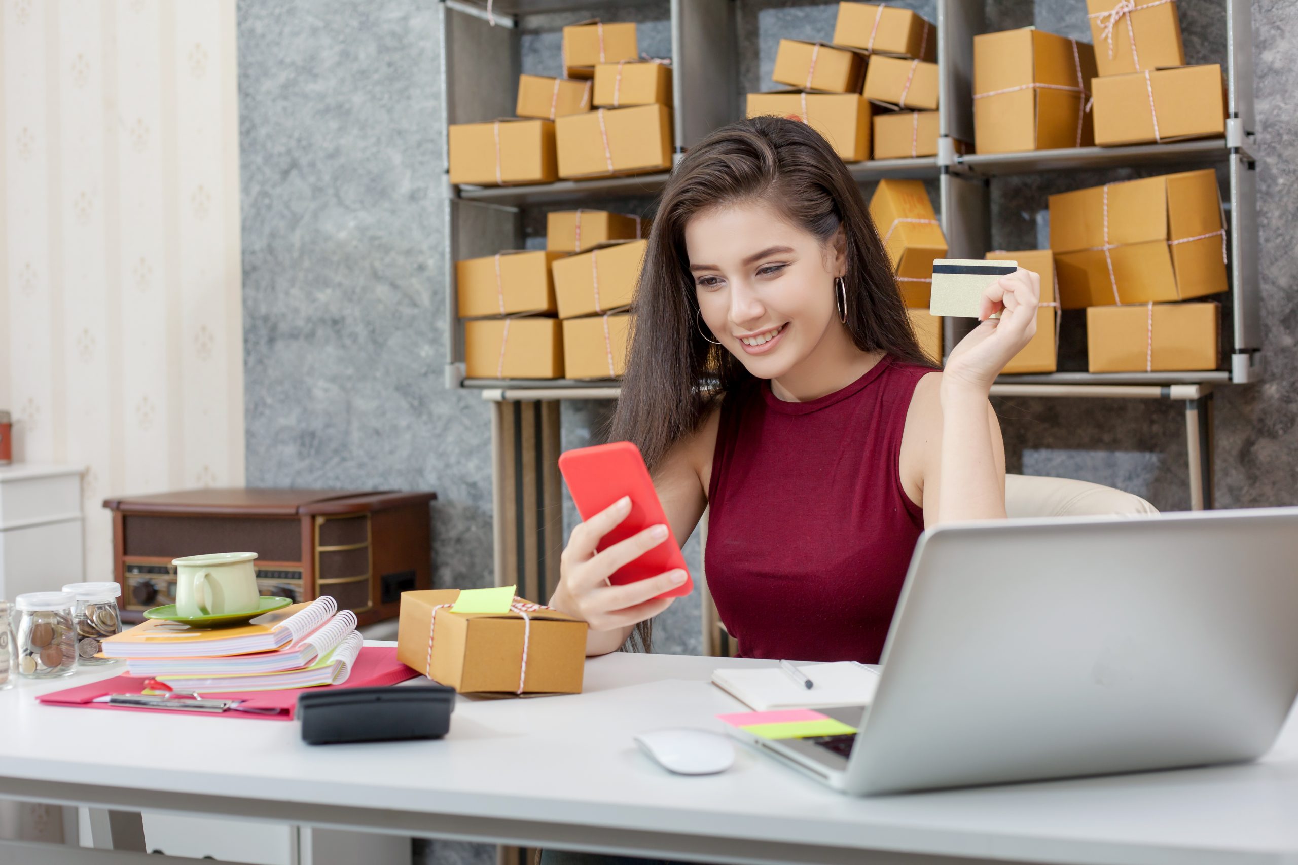 Young woman using smartphone for SMS marketing Malaysia e-commerce orders while holding a credit card at her desk