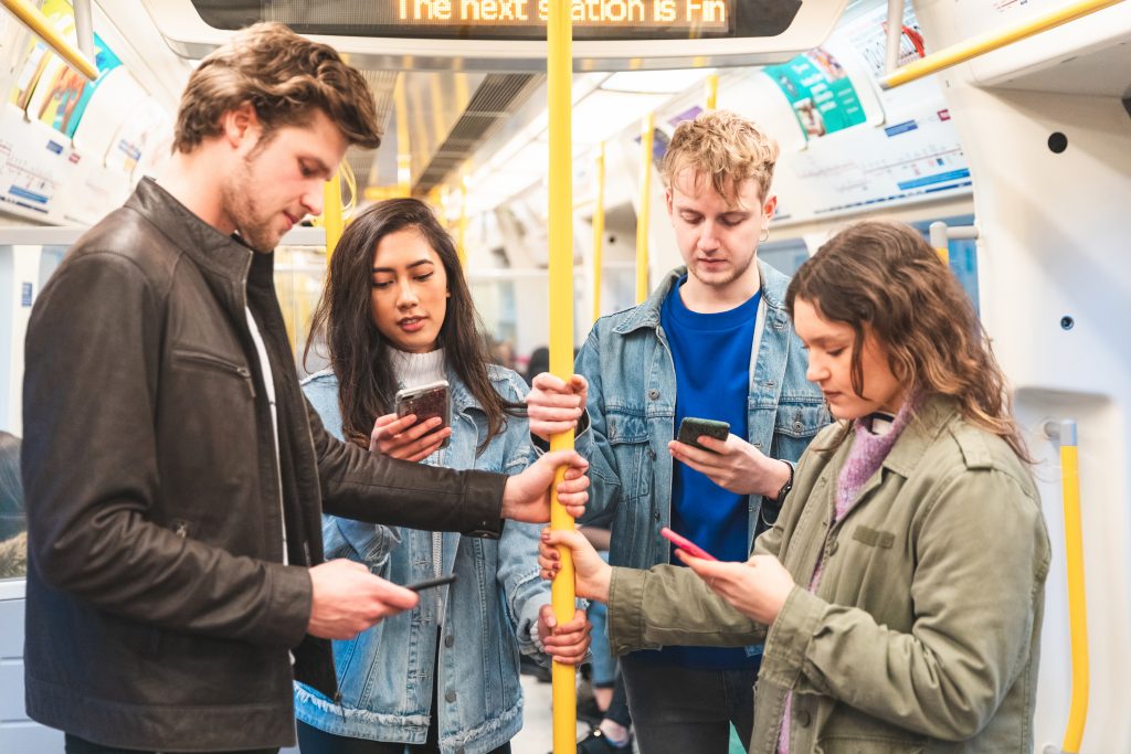 Young commuters checking their smartphones on public transport, showing how Bulk SMS Malaysia messages reach users instantly on mobile devices.