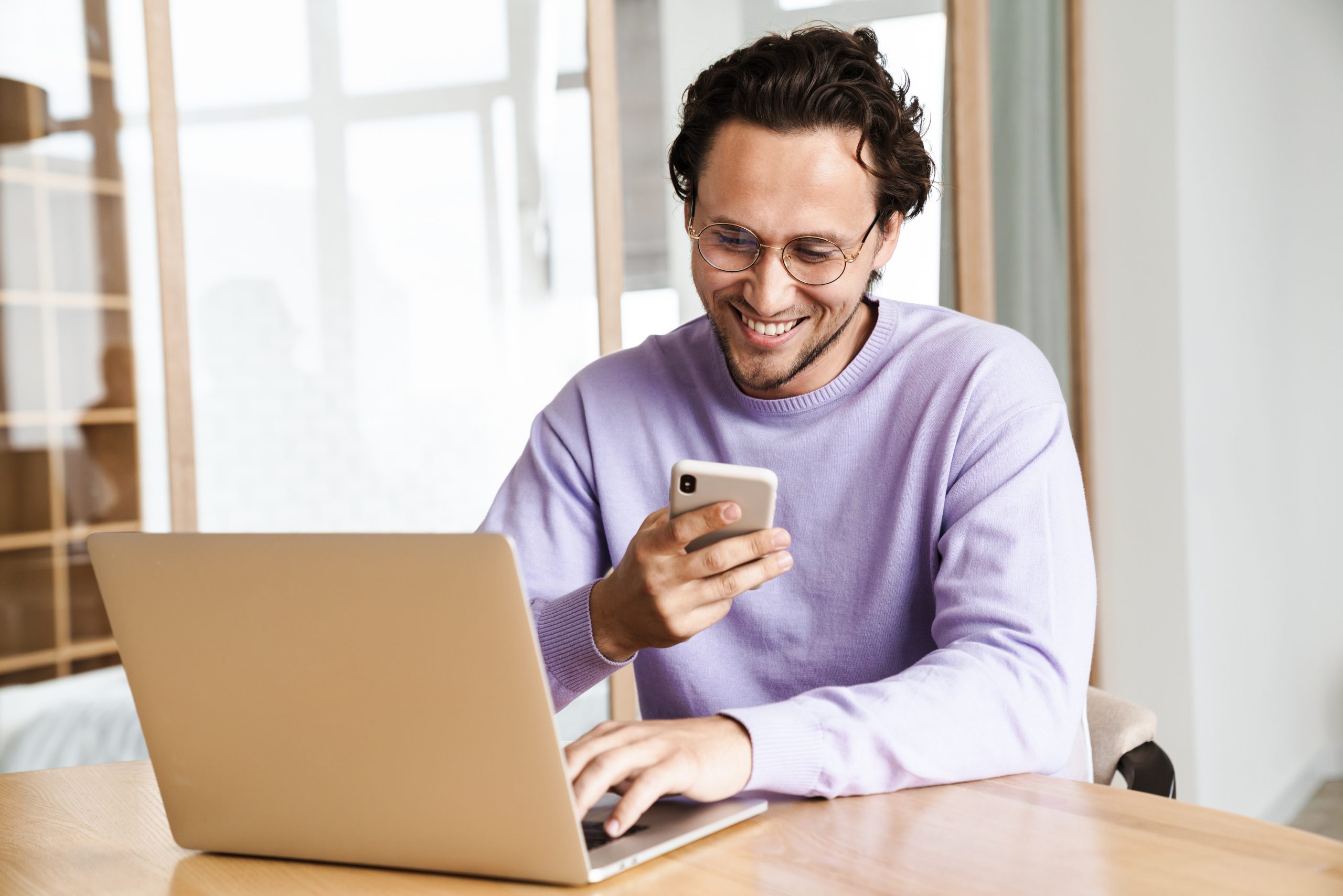 Business professional checking a smartphone while working on a laptop, showing real-time engagement using a send SMS API