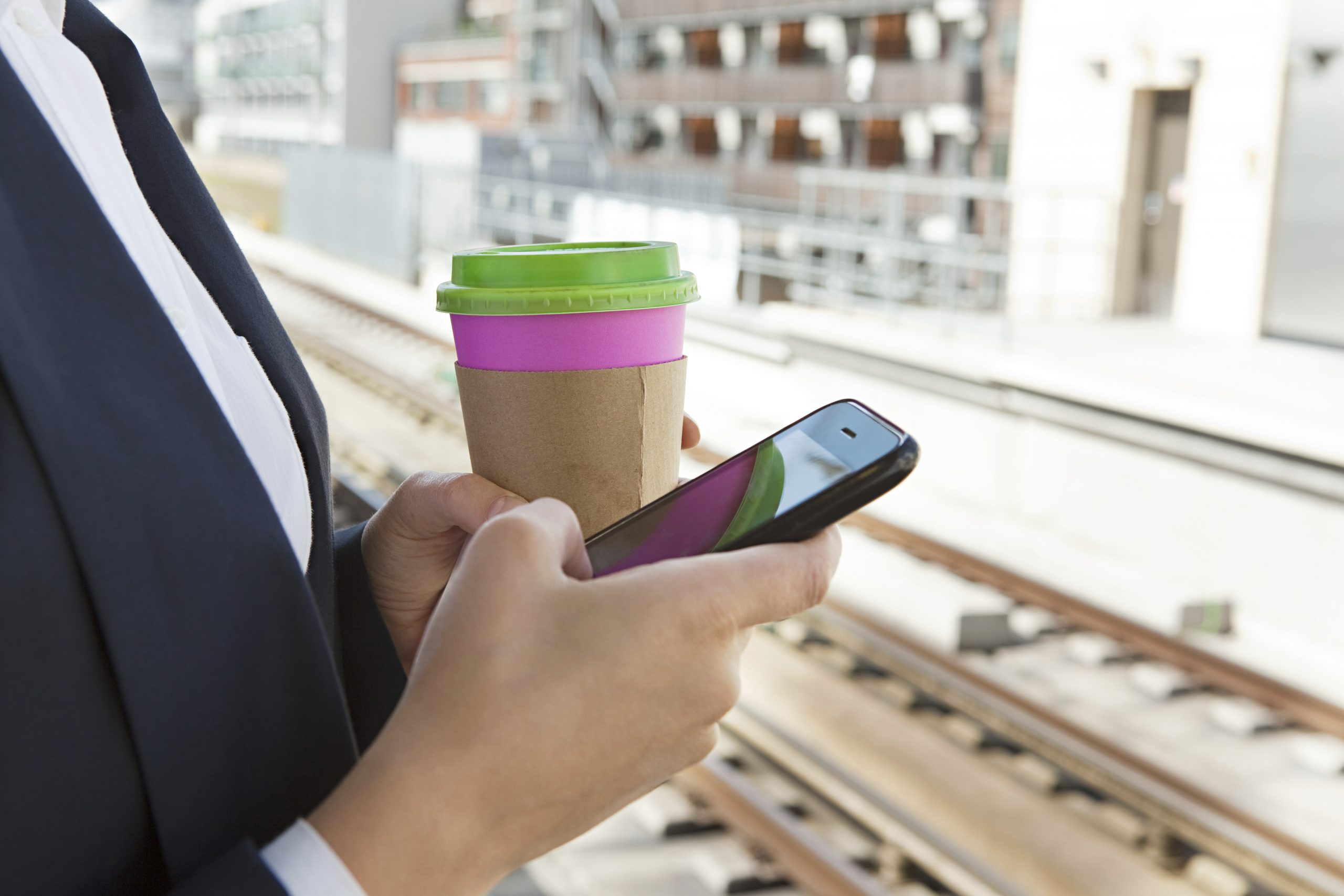 Business professional checking smartphone on train platform, illustrating send SMS API real-time alerts