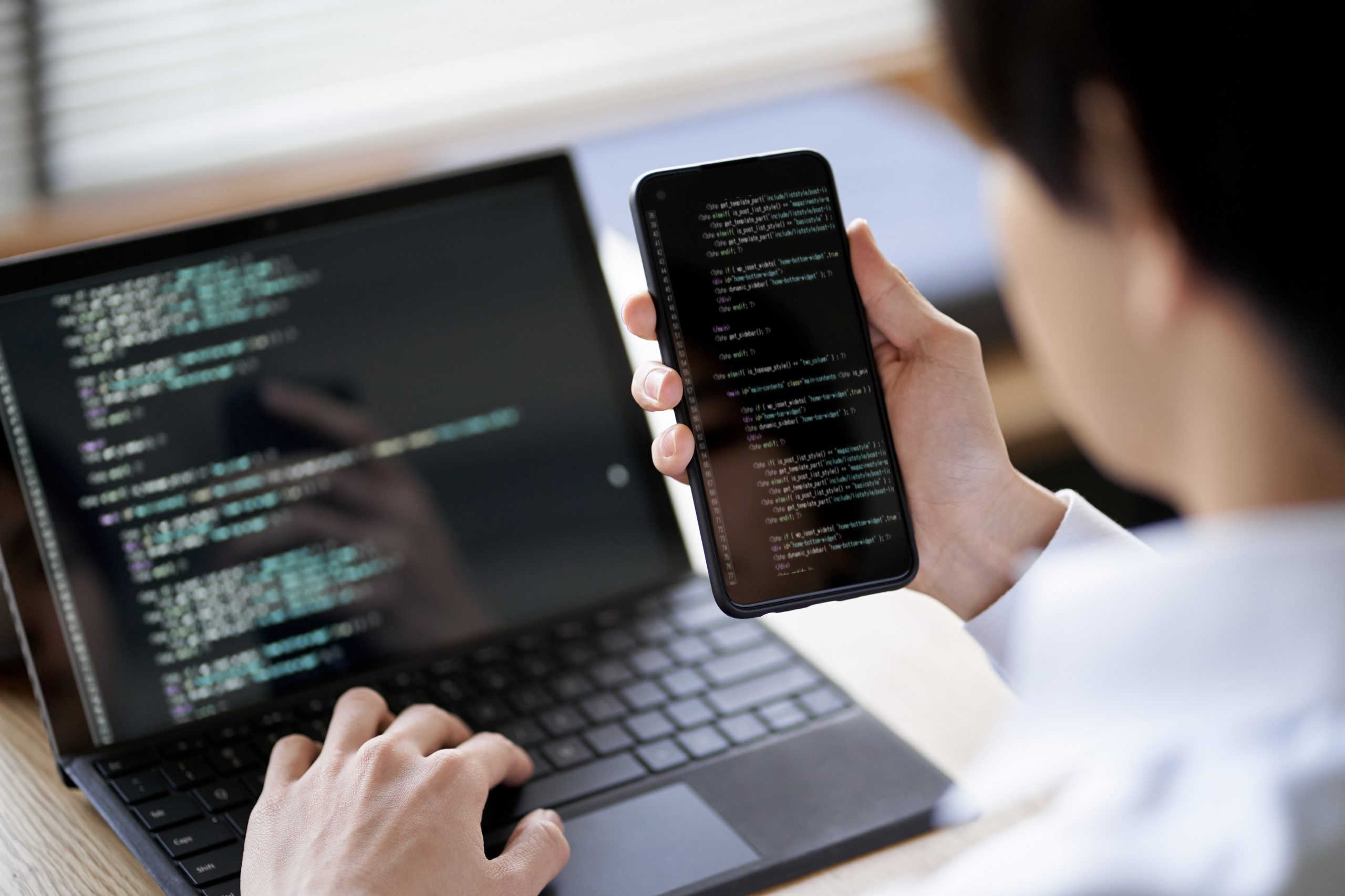 Developer testing SMS Gateway Provider API on smartphone while coding on laptop