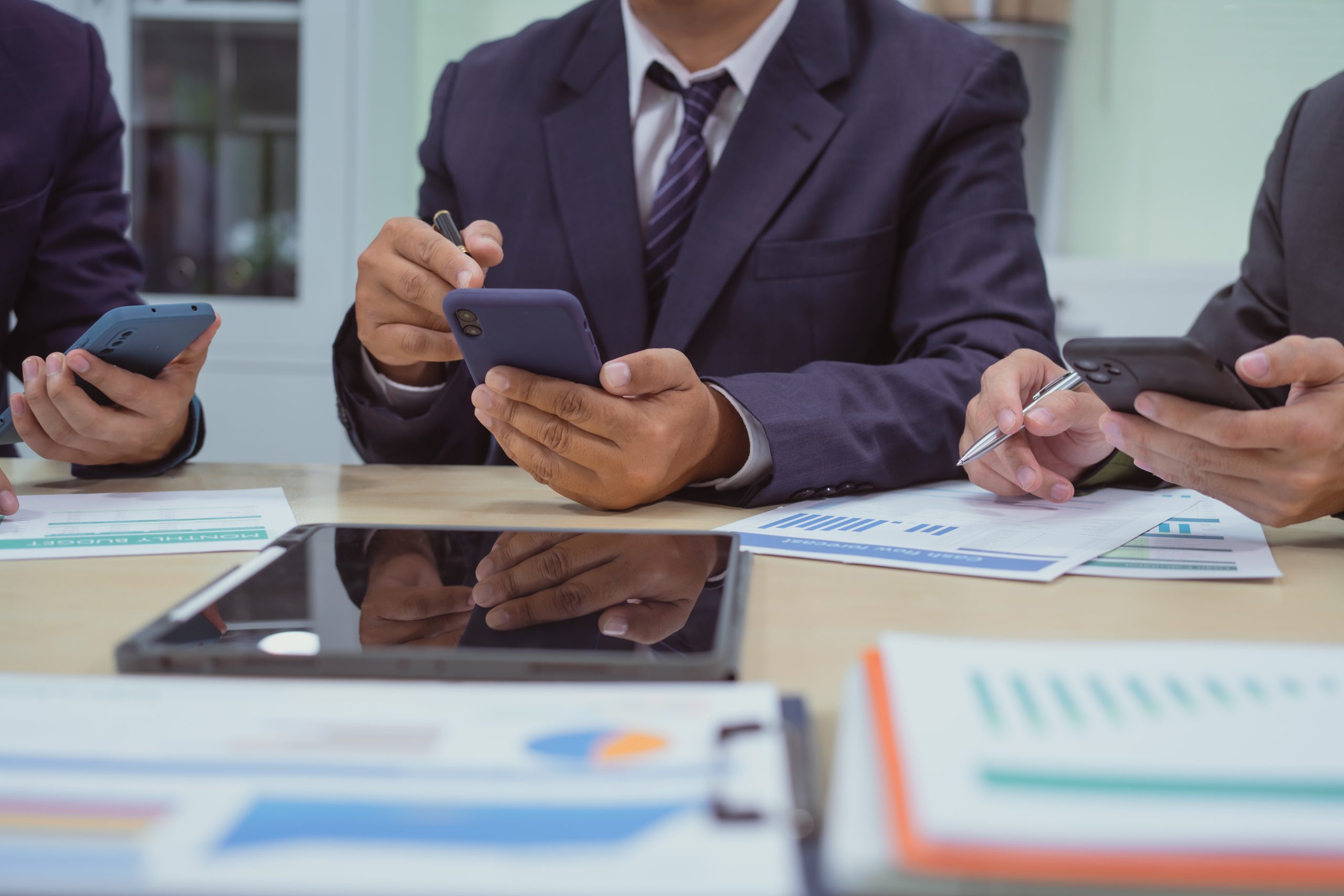 Business team using mobile devices to automate workflows with a send SMS API during a meeting.