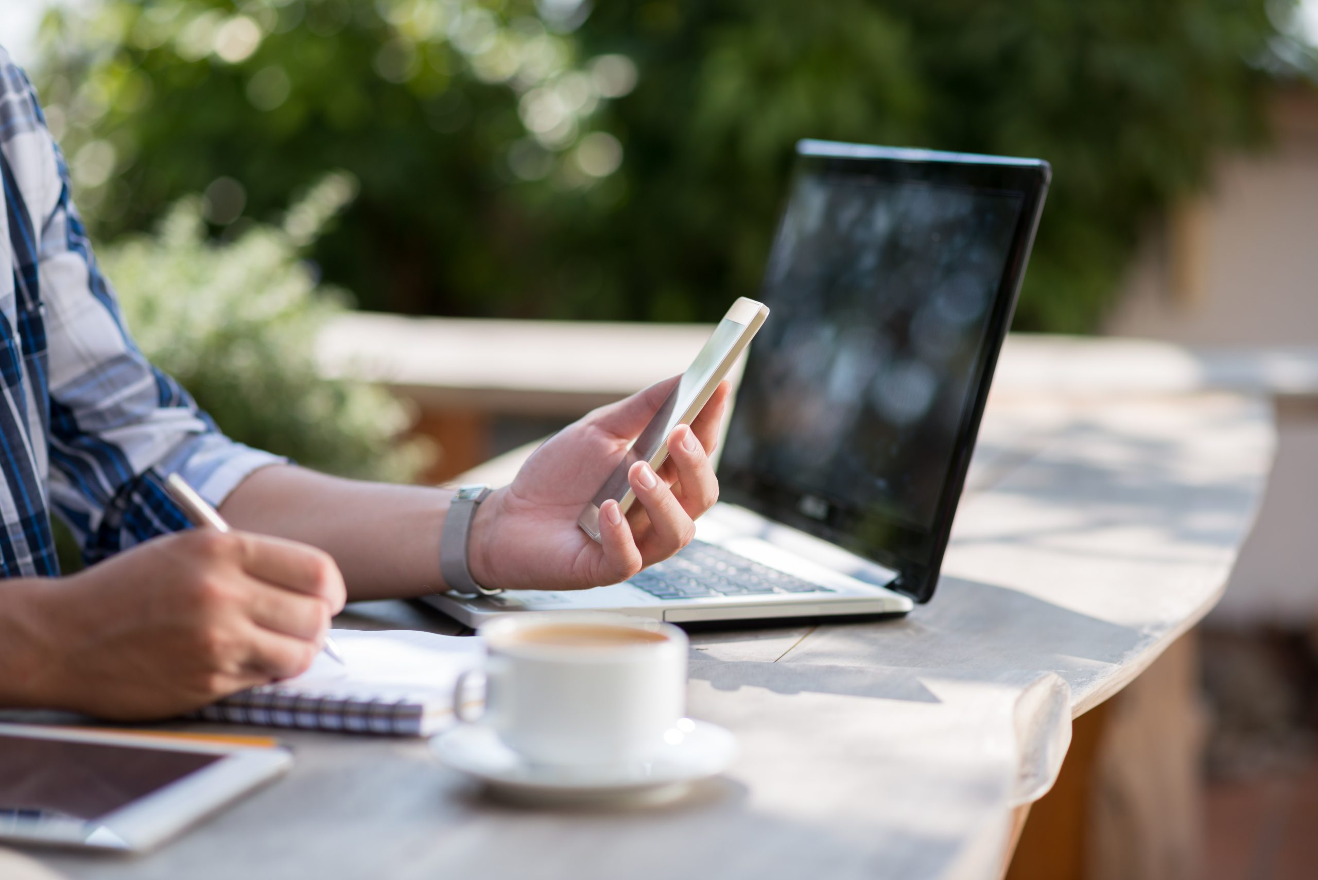 Person using a smartphone beside a laptop while working at a table
