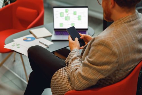 Enterprise professional using a smartphone with business system workflow on laptop