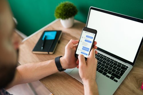 Developer using WhatsApp messaging on a mobile phone with a laptop