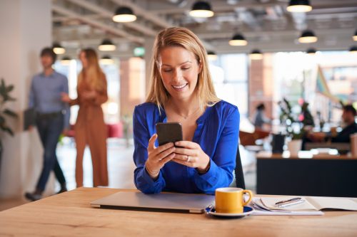 Professional woman receiving a notification from a Bulk SMS Malaysia service on her smartphone at work.